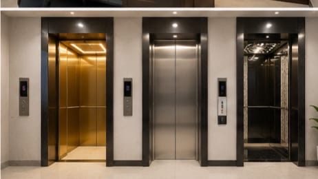 Three finished elevator cabins — brass, brushed steel and mirrored finishes — installed in a building lobby